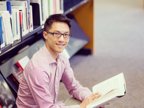 Feliz estudiante masculino sosteniendo libros en la biblioteca — Foto de Stock
