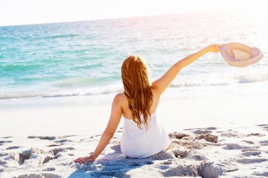 Genç bir kadın sahilde oturuyor.