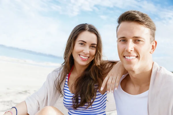 Romantische jonge paar zittend op het strand — Stockfoto