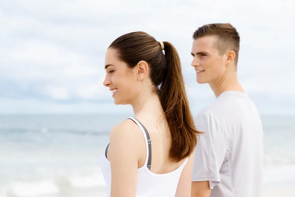 Ungt par ser betænksom ud, mens de står ved siden af hinanden på stranden - Stock-foto