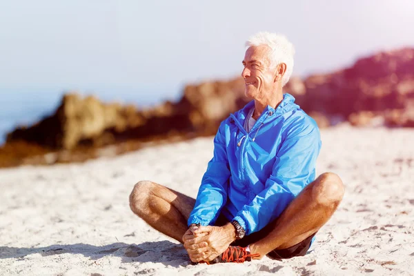 Mannen i sportkläder sitter på stranden — Stockfoto