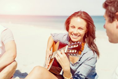 Güzel genç bir kadın sahilde gitar çalıyor.