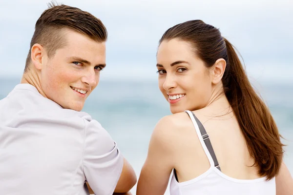 Young couple looking at camera while sitting next to each other on beach — Stock Photo, Image