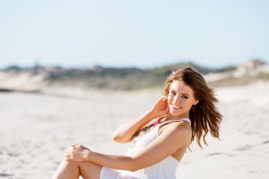 Genç bir kadın sahilde oturuyor.