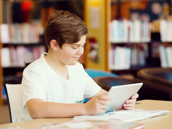 Мальчик-подросток с планшетом в библиотеке — стоковое фото