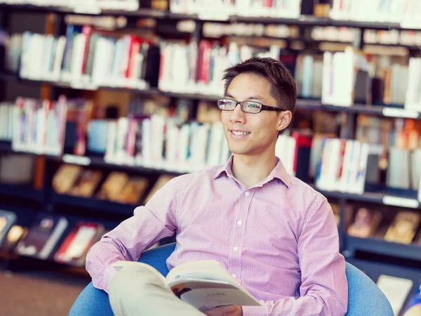 Glücklicher männlicher Student mit Büchern in der Bibliothek — Stockfoto