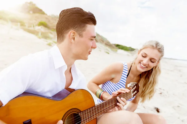 Pareja joven tocando la guitarra en la playa enamorada — Foto de Stock