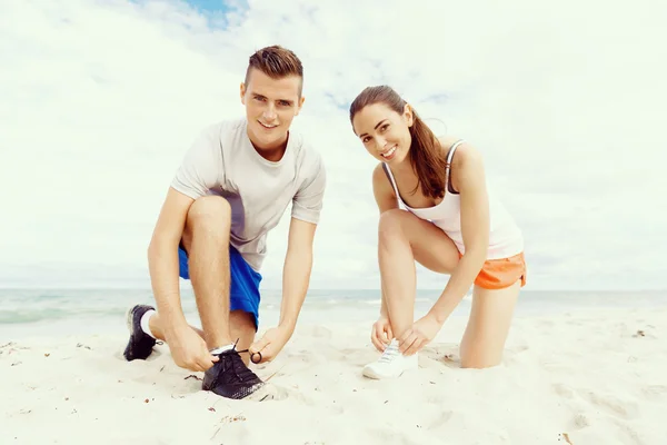 Corredores. Jovem casal exercitando e stertching na praia — Fotografia de Stock
