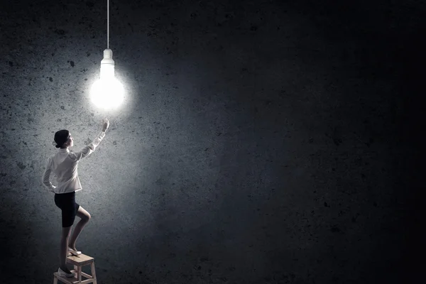 Businesswoman reaching light bulb — Stock Photo, Image