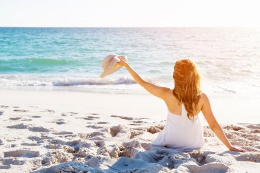 Genç bir kadın sahilde oturuyor.