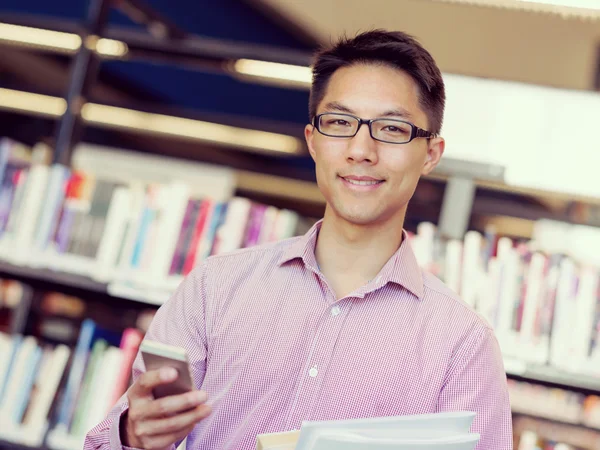 Glücklicher männlicher Student mit Büchern in der Bibliothek — Stockfoto