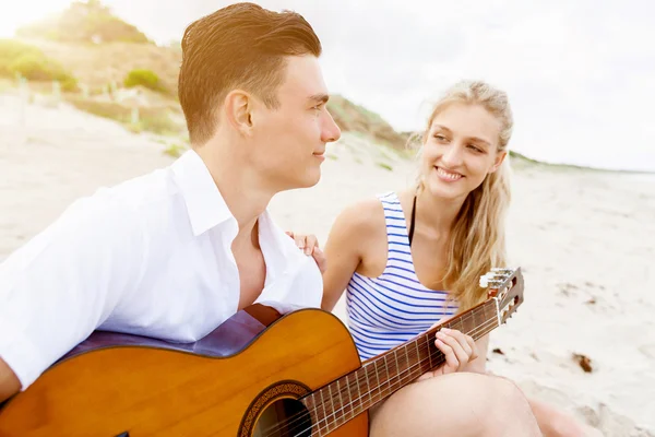 Pareja joven tocando la guitarra en la playa enamorada —  Fotos de Stock