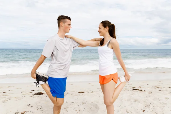 Corredores. Jovem casal exercitando e stertching na praia — Fotografia de Stock