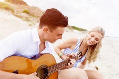 Genç çift aşık sahilde gitar çalmak