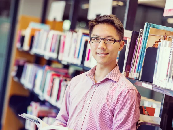 Glücklicher männlicher Student mit Büchern in der Bibliothek — Stockfoto