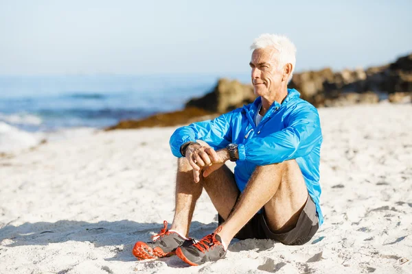Мужчина в спортивной одежде сидит на пляже — стоковое фото