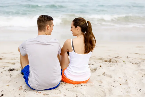 Młoda para spogląda na siebie siedząc na plaży — Zdjęcie stockowe