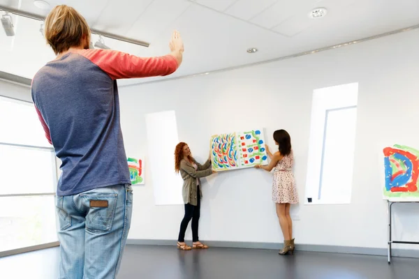 Jovens artistas na galeria pendurado pintura nas paredes — Fotografia de Stock