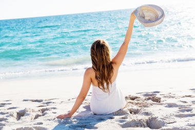 Genç bir kadın sahilde oturuyor.