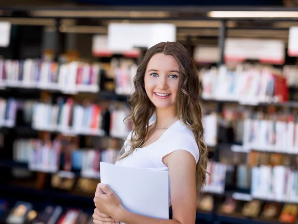 Lykkelig kvinnelig student som holder bøker på biblioteket – stockfoto