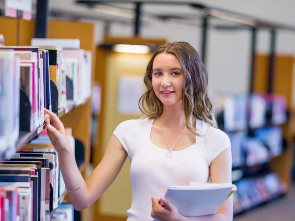Glad kvinnlig student håller böcker på biblioteket — Stockfoto