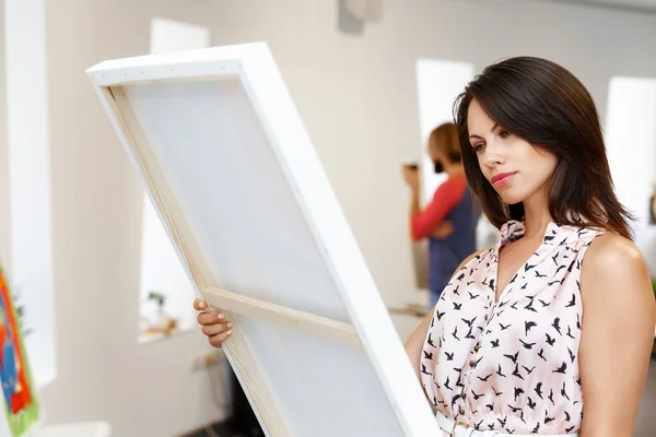 Junge kaukasische Frau steht in Kunstgalerie vor Gemälden — Stockfoto