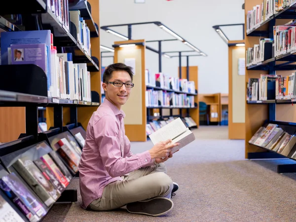 Glücklicher männlicher Student mit Büchern in der Bibliothek — Stockfoto