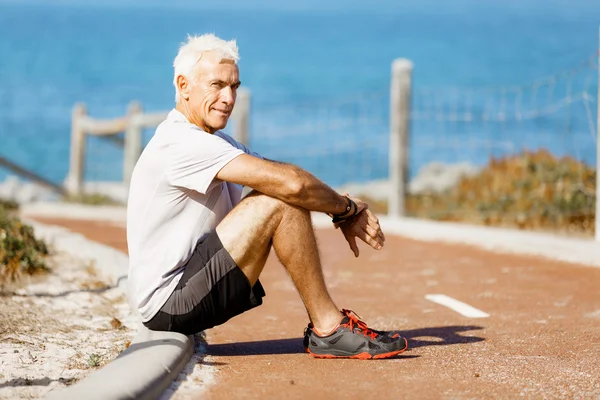 Mannen i sportkläder sitter på stranden — Stockfoto