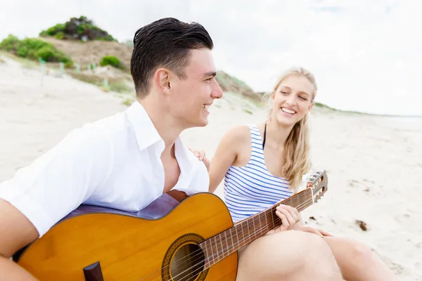 Pareja joven tocando la guitarra en la playa enamorada —  Fotos de Stock