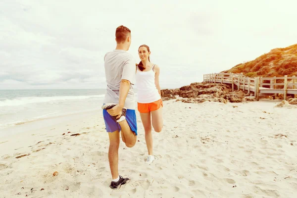 Corredores. Pareja joven haciendo ejercicio y esteretizando en la playa — Foto de Stock