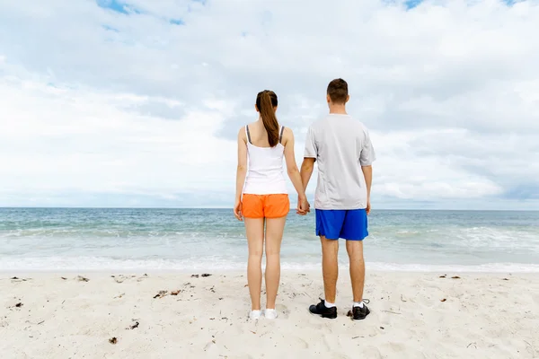 Junges Paar schaut nachdenklich, während es nebeneinander am Strand steht — Stockfoto