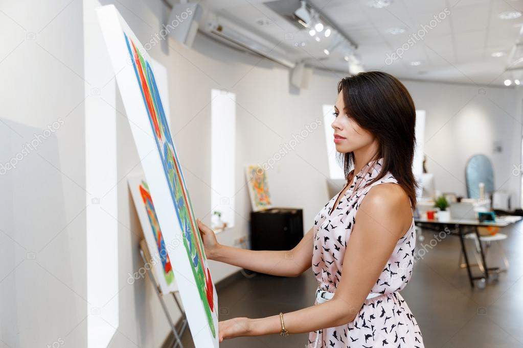 Young caucasian woman standing in art gallery front of  paintings