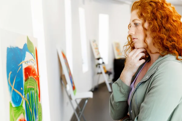 Giovane donna caucasica in piedi in galleria d'arte davanti a dipinti — Foto Stock