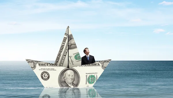 Бизнесмен в лодке из долларовой купюры — стоковое фото