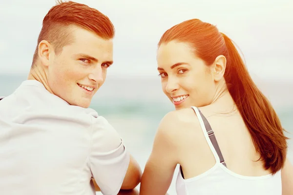 Молодая пара смотрит в камеру, сидя на пляже — стоковое фото