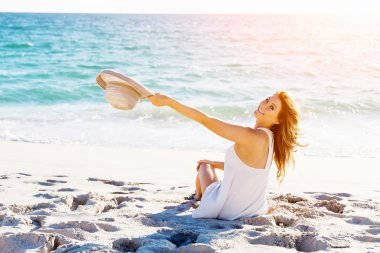 Genç bir kadın sahilde oturuyor.