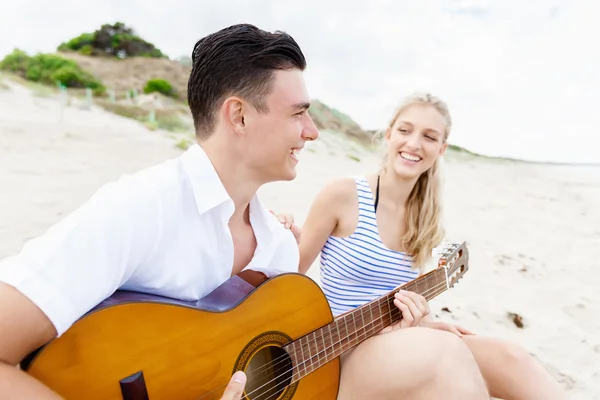 Pareja joven tocando la guitarra en la playa enamorada —  Fotos de Stock