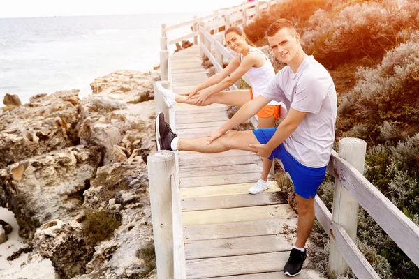 Corredores. Pareja joven haciendo ejercicio y esteretizando en la playa —  Fotos de Stock