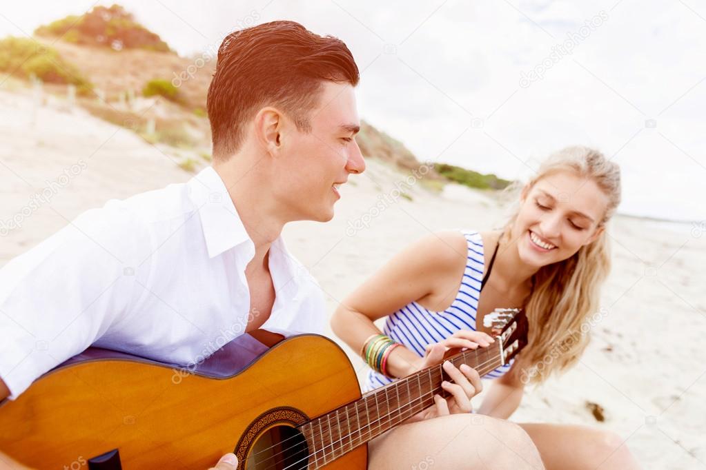 Young couple playing guitar on beach in love