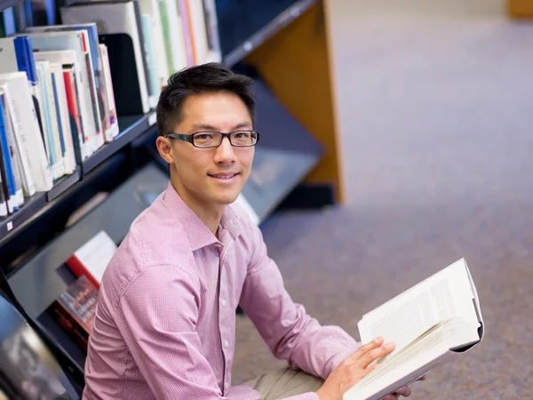 Glücklicher männlicher Student mit Büchern in der Bibliothek — Stockfoto