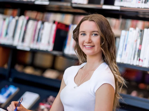 Happy female student holding books at the library — Stock Photo, Image