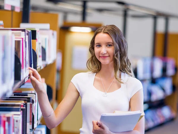 Feliz estudiante sosteniendo libros en la biblioteca — Foto de Stock