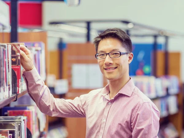 Šťastný muž student vyzvednutí knih v knihovně — Stock fotografie