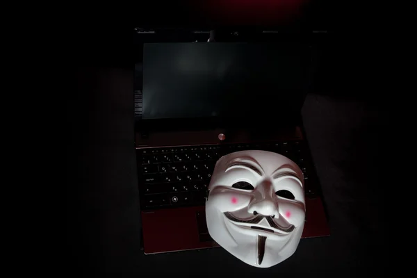 Anonieme masker donkere over laptop — Stockfoto