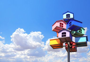 Mavi gökyüzü arka planında renkli yuva kutuları. Farklı renklerde kuş evleri ve bulutlu mavi gökyüzü.