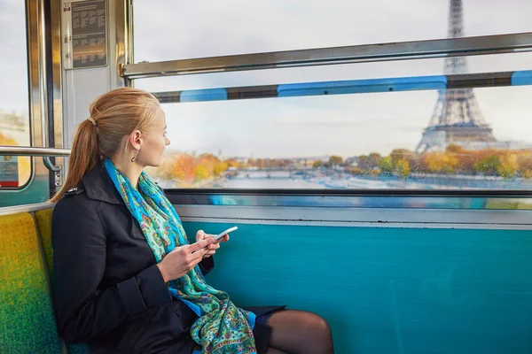 Hermosa joven viajando en un tren de metro parisino y usando su teléfono móvil — Foto de Stock