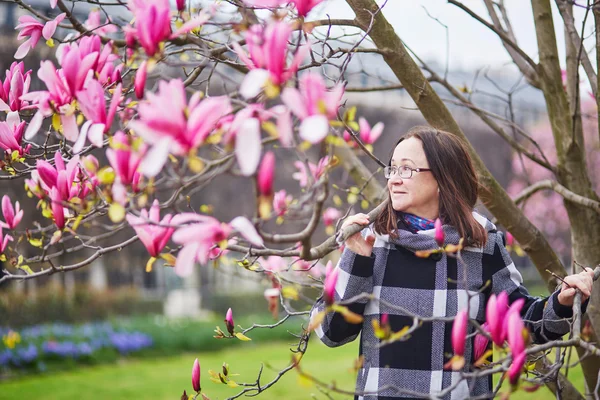 Beautiful middle aged admiring pink magnolia — Stock Photo, Image