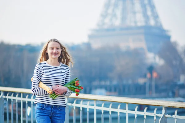 Schönes junges Mädchen mit Baguette und Tulpen in der Nähe des Eiffelturms — Stockfoto