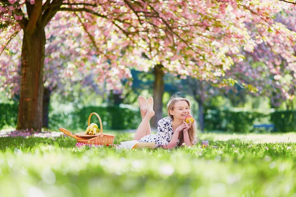 Beautiful young woman having picnic in blooming spring park — Stock Photo, Image