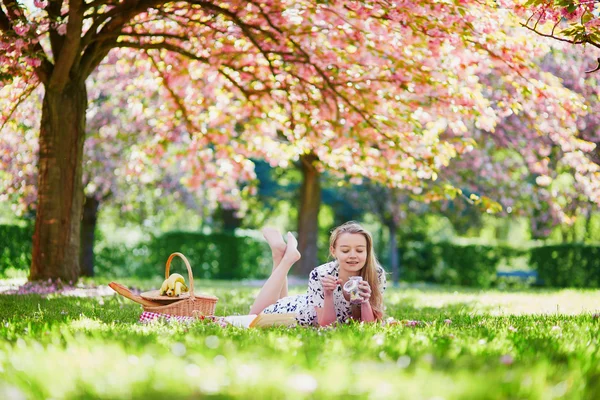 Vacker ung kvinna ha picknick under blommande våren park — Stockfoto